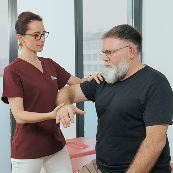 Orthopädin Frau Dr. Limbrock führt eine manuelle Untersuchung am Arm eines sitzenden Patienten durch.