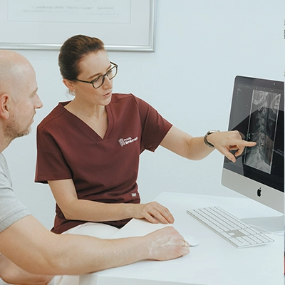 Frau Dr. Limbrock zeigt auf ein digitales Röntgenbild und erläutert die Befunde im Gespräch mit einem Patienten.